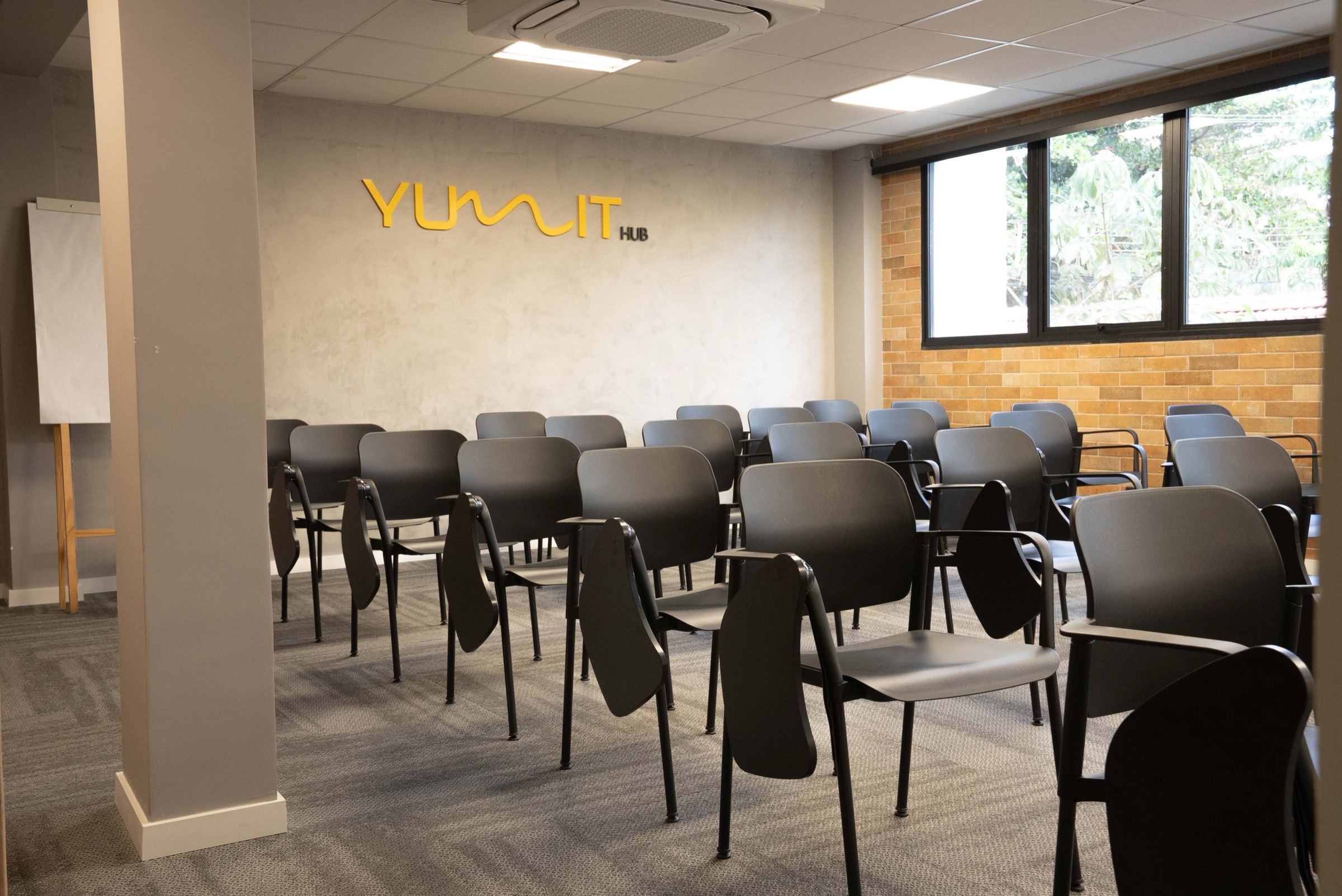 Sala de Treinamento do Yumit Hub — fileiras de cadeiras universitárias, lousa e tela interativa HD para workshops e turmas